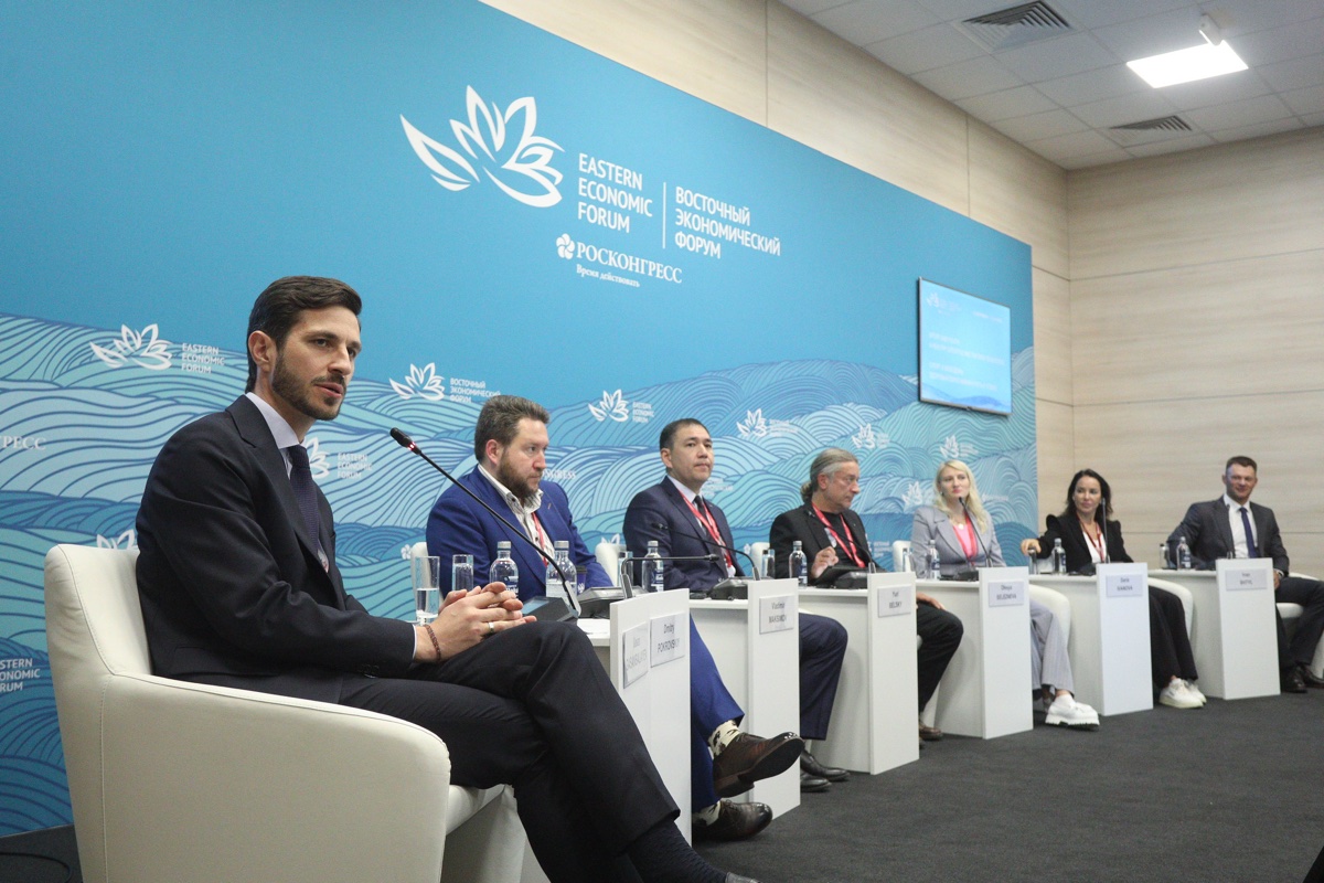 Спикеры панели сидят на синей брендированной сцене форума.
