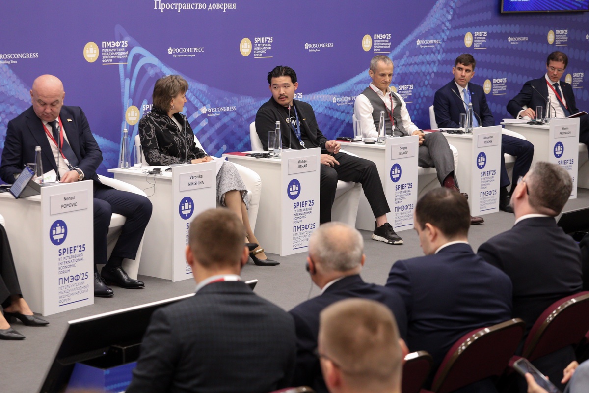 Широкий вид панели форума со спикерами и аудиторией на переднем плане.