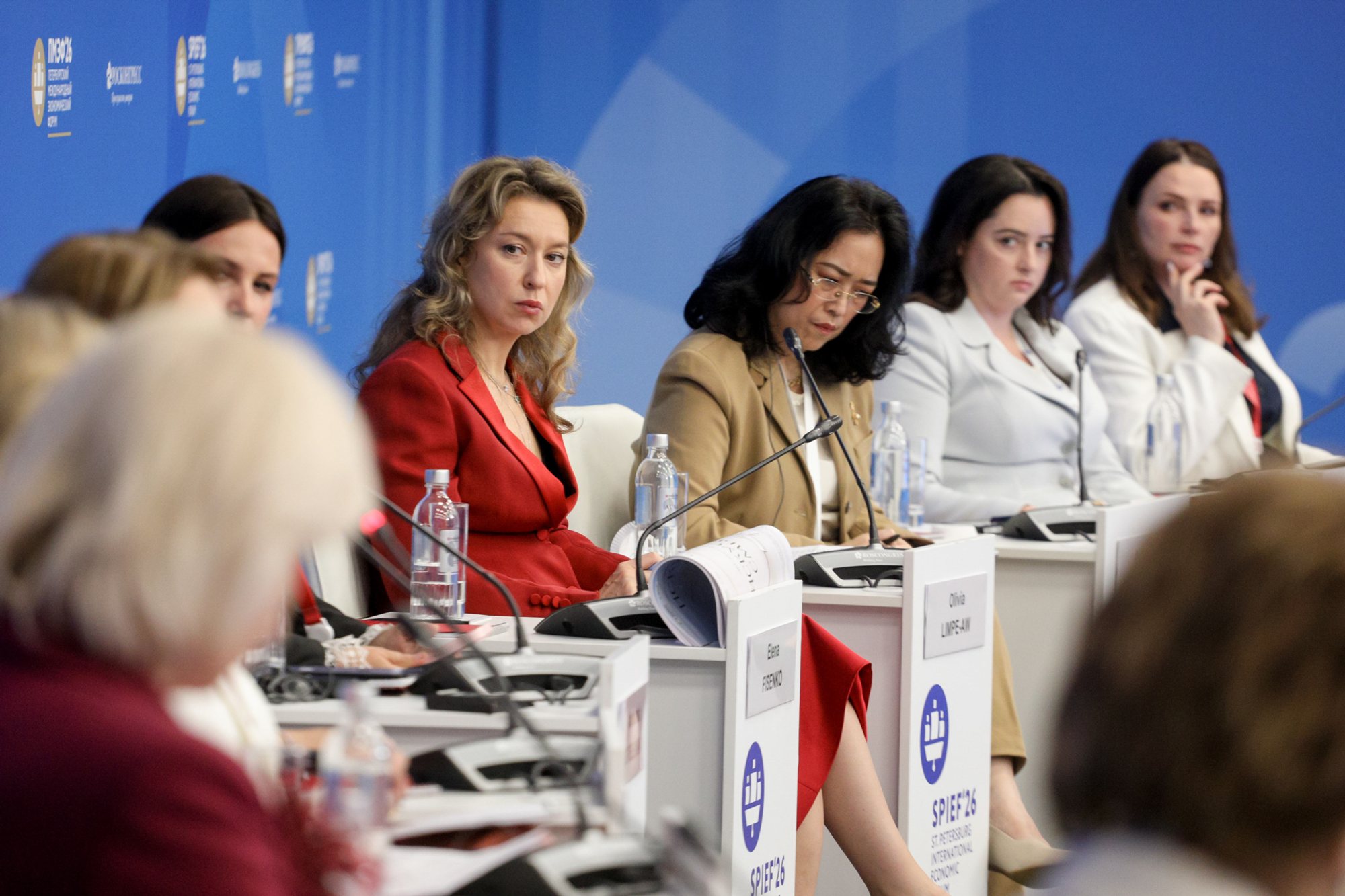 Five people seated at a long conference table with microphones, nameplates and water bottles; blue ExpoForum event backdrop with logos.