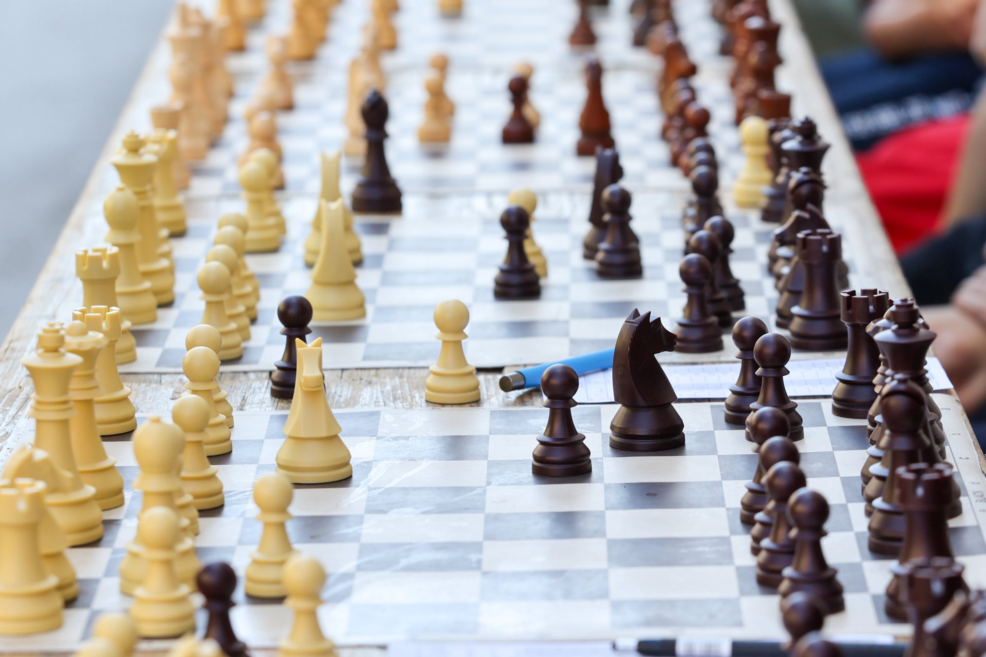 Long row of chessboards on a table with white and dark pieces arranged for play on Subotički Korzo; shallow depth of field.