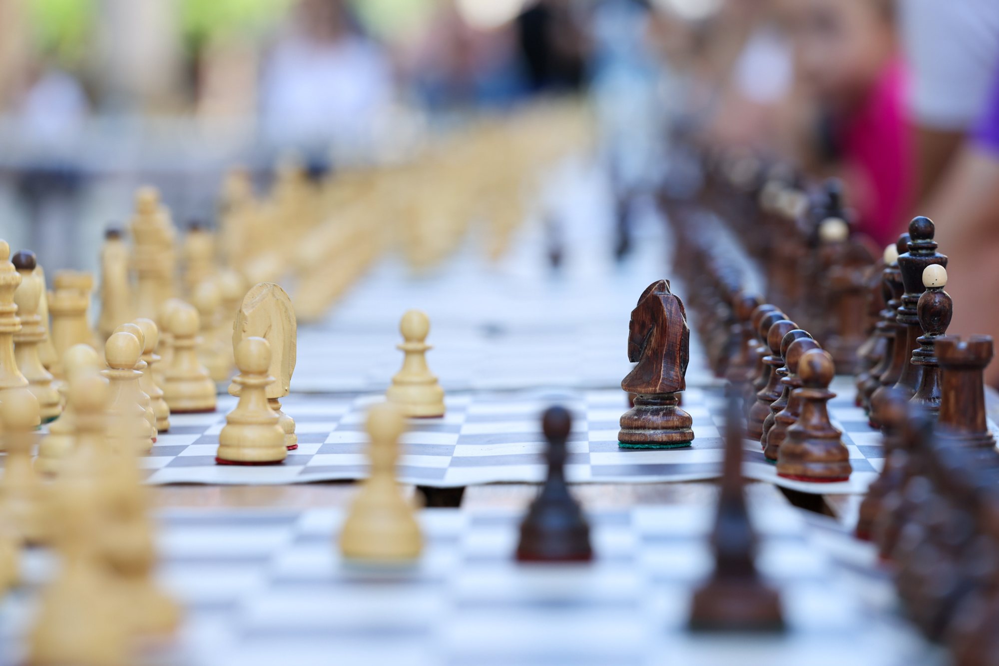 Line of chessboards on a long table with white and dark pieces; nearest boards in sharp focus while others blur into the distance.