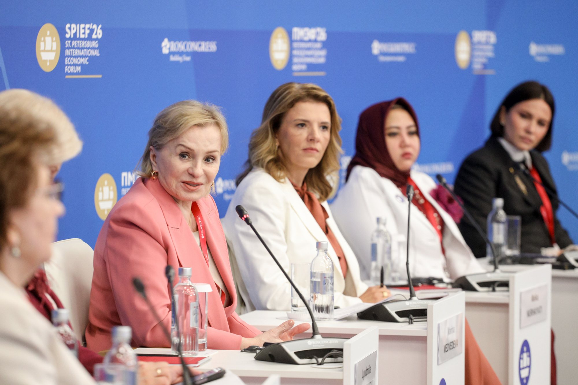 Five panel participants seated behind a white conference table with microphones, bottled water and nameplates, against a blue St. Petersburg International Economic Forum (SPIEF) backdrop.